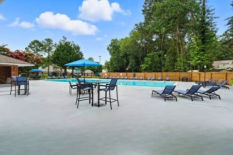 A pool with chairs and umbrellas is surrounded by a fence.