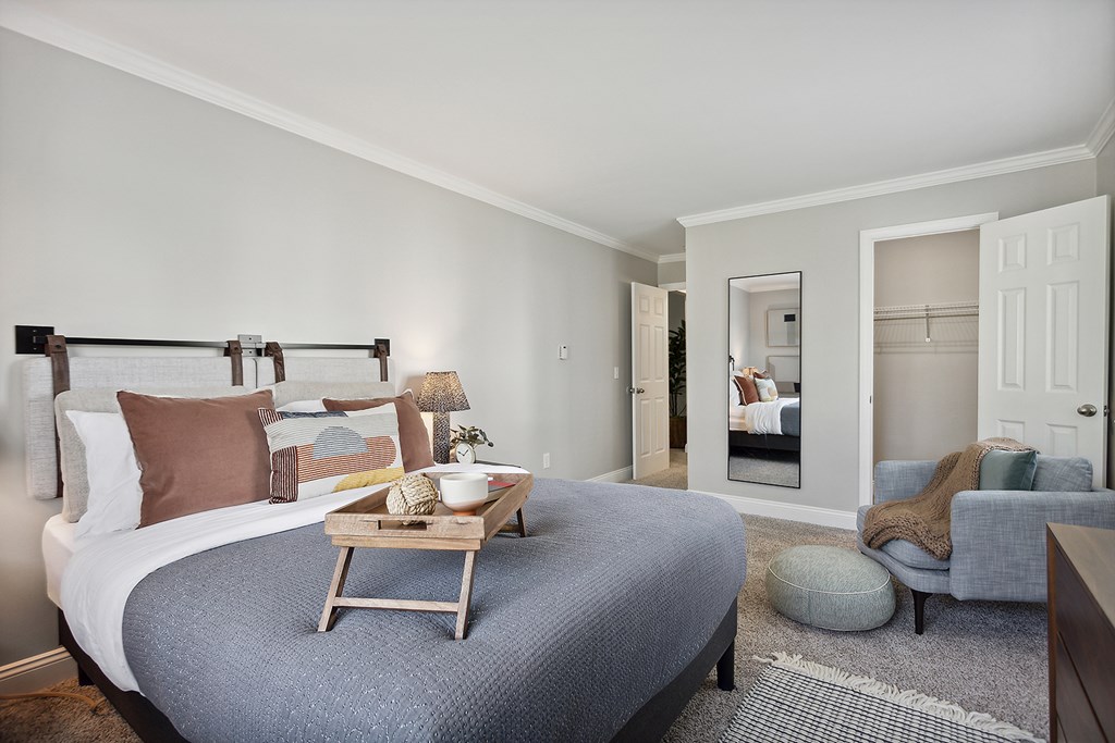 A bedroom with a bed, a chair, and a mirror.