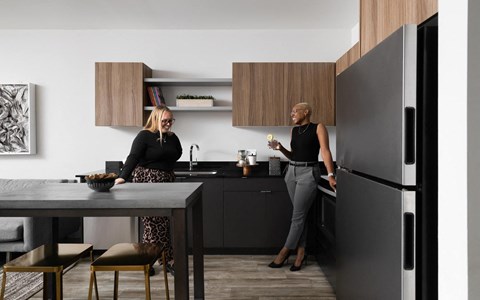 two women in a kitchen with a refrigerator and a table