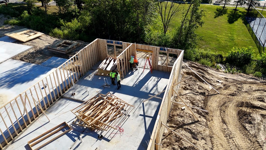 A construction site with a partially built wooden structure and a worker in the middle.