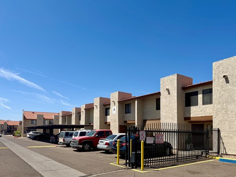 A parking lot with cars and a gated entrance to apartment buildings.