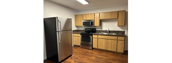 A kitchen with a black refrigerator, stainless steel oven, microwave, and wooden cabinets.