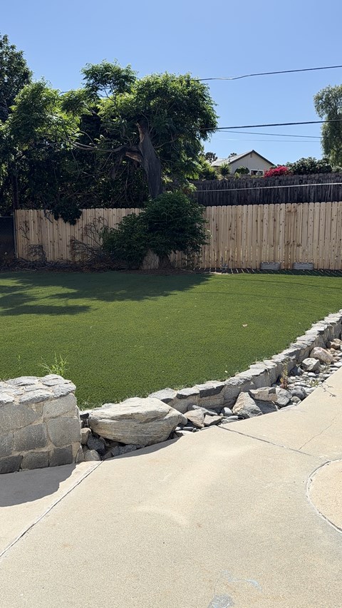 A backyard with a stone wall and a green lawn.