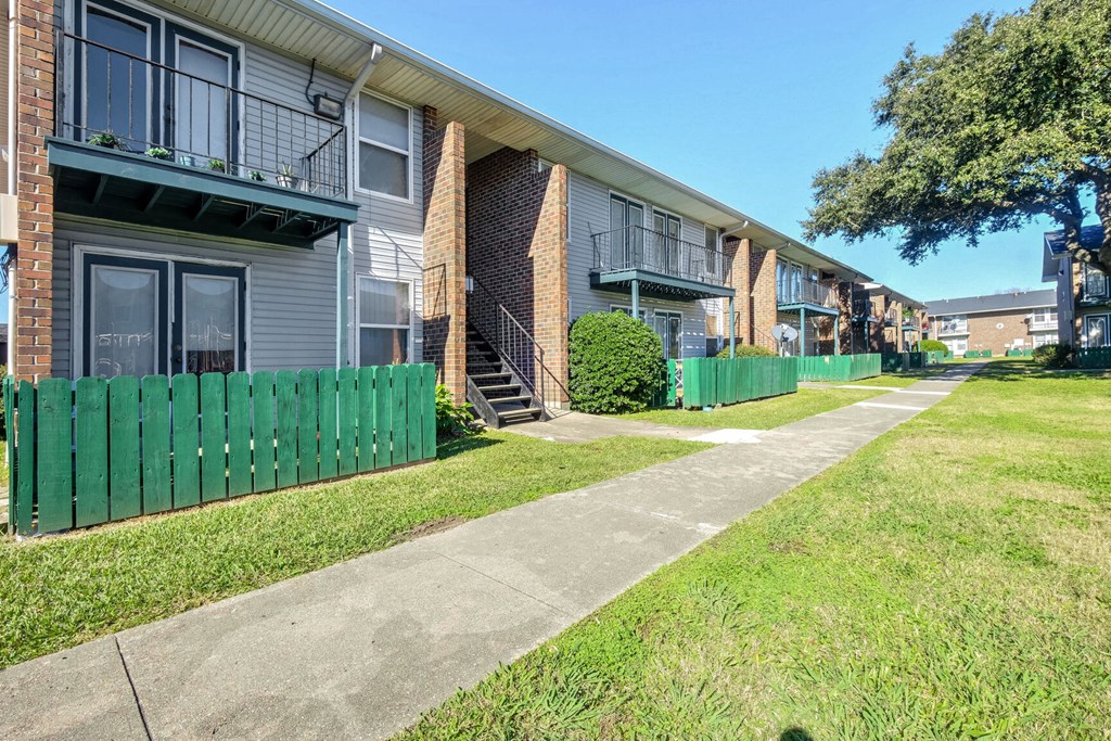 A row of apartment buildings with green fences and a sidewalk in front.