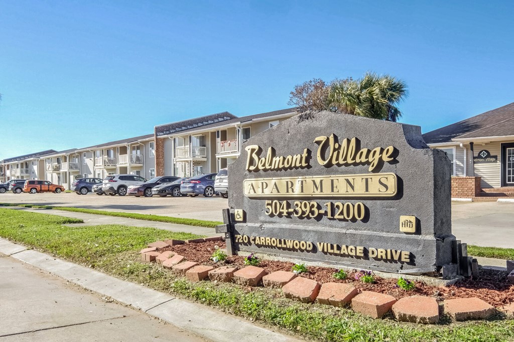 A sign for Belmont Village Apartments is in front of a row of houses.