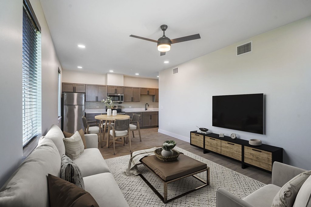 A modern living room with a flat screen TV and a kitchen area in the background.