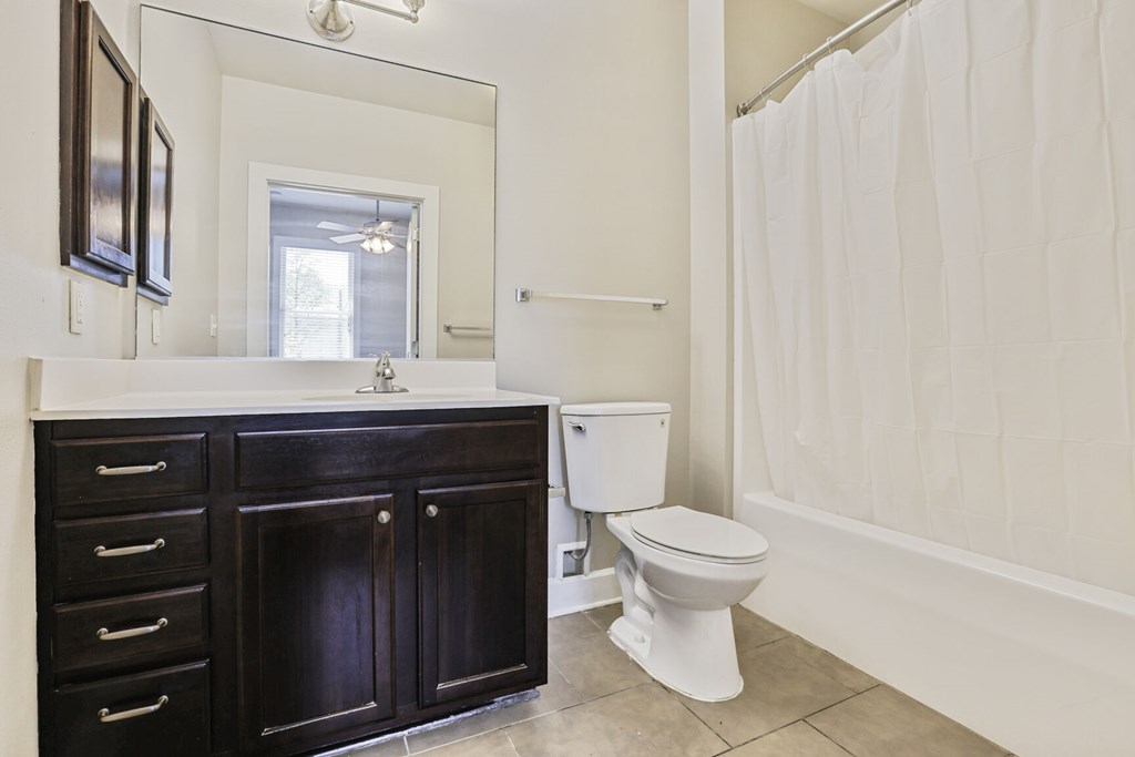 A white toilet sits in a bathroom with a white shower curtain.