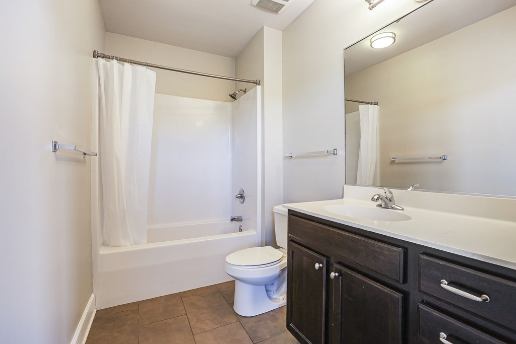 A white toilet sits in a bathroom next to a sink and a bathtub.
