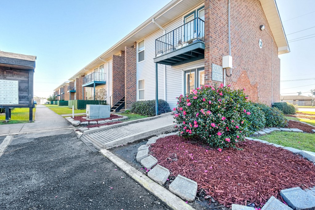 A red brick building with a balcony and a flower bed in front.