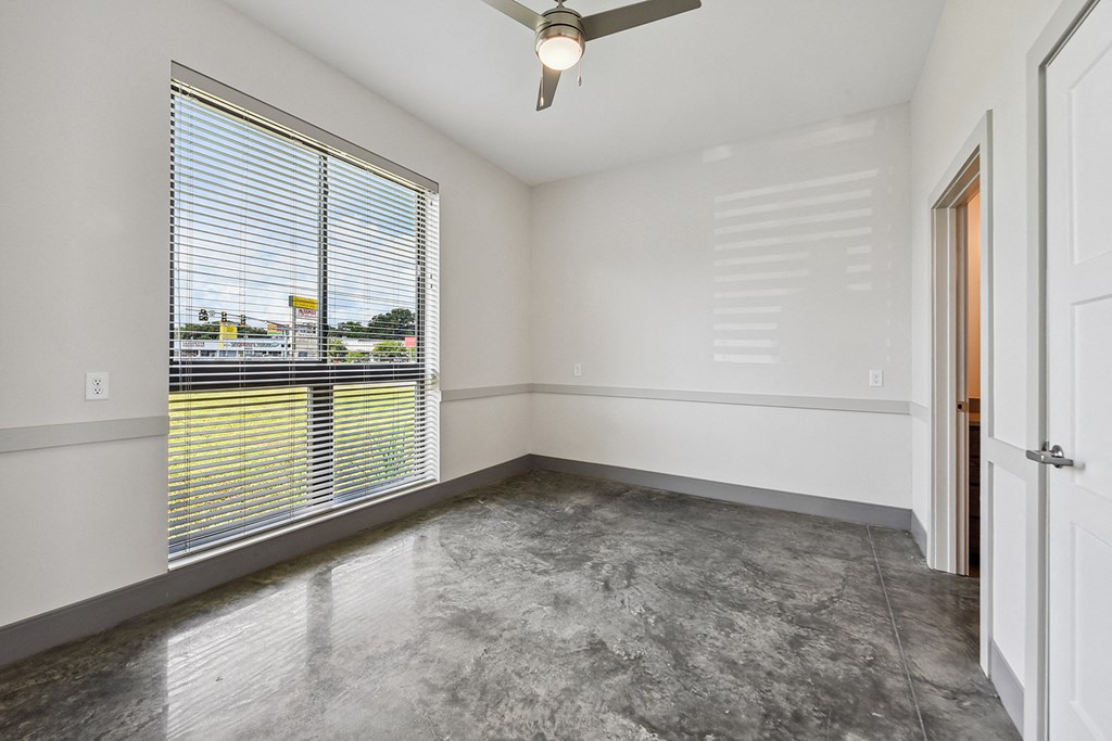 the living room of an apartment with a large window and concrete floor