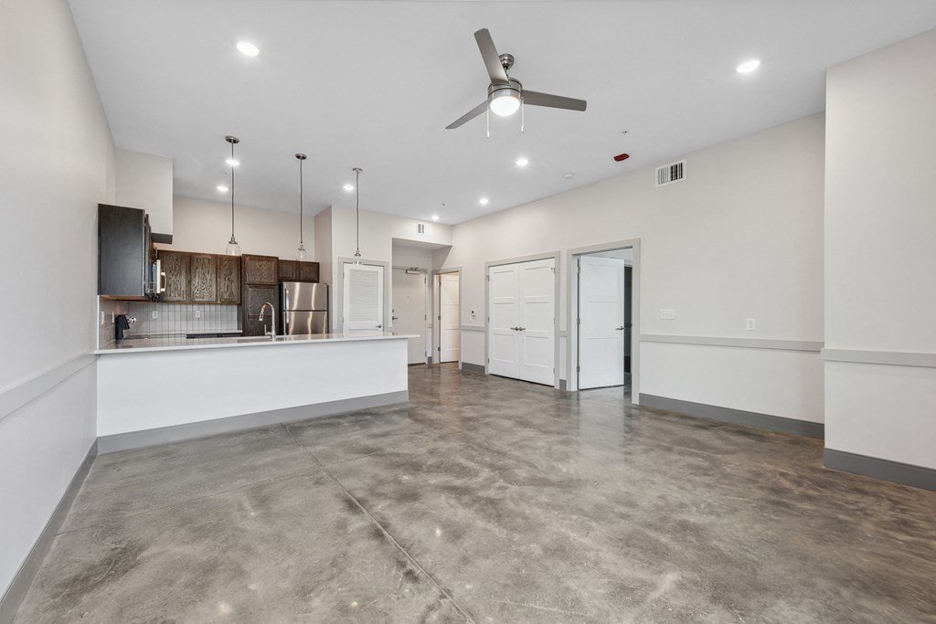 an empty living room with a kitchen and a ceiling fan