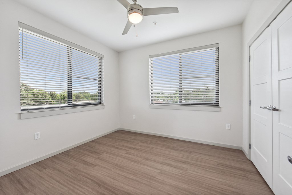 an empty bedroom with a ceiling fan and two windows