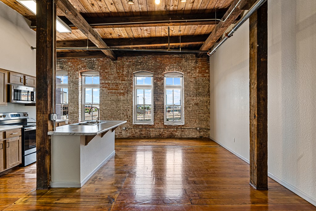 an empty room with a kitchen and exposed brick walls and wood floors