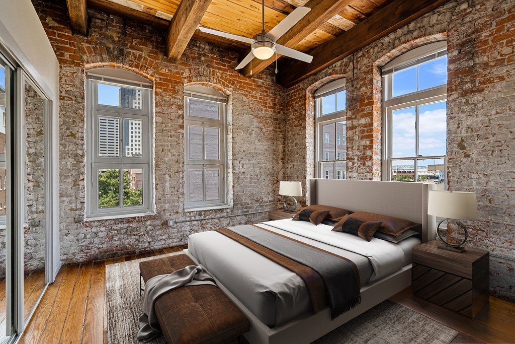 an exposed brick bedroom with a bed and windows