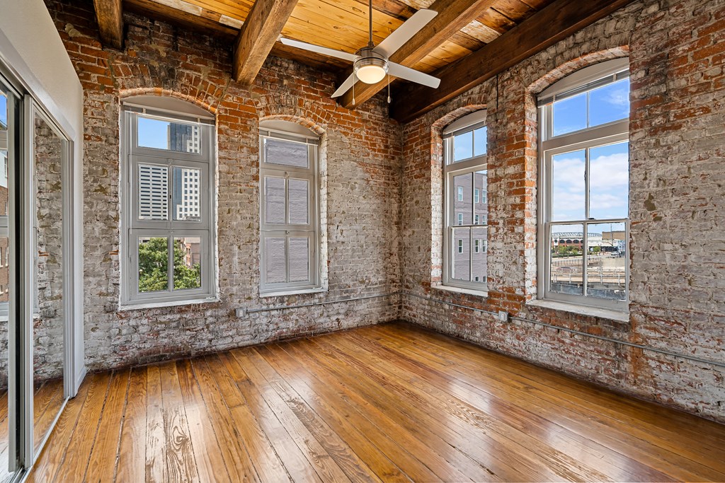 an empty room with brick walls and wood floors and a ceiling fan