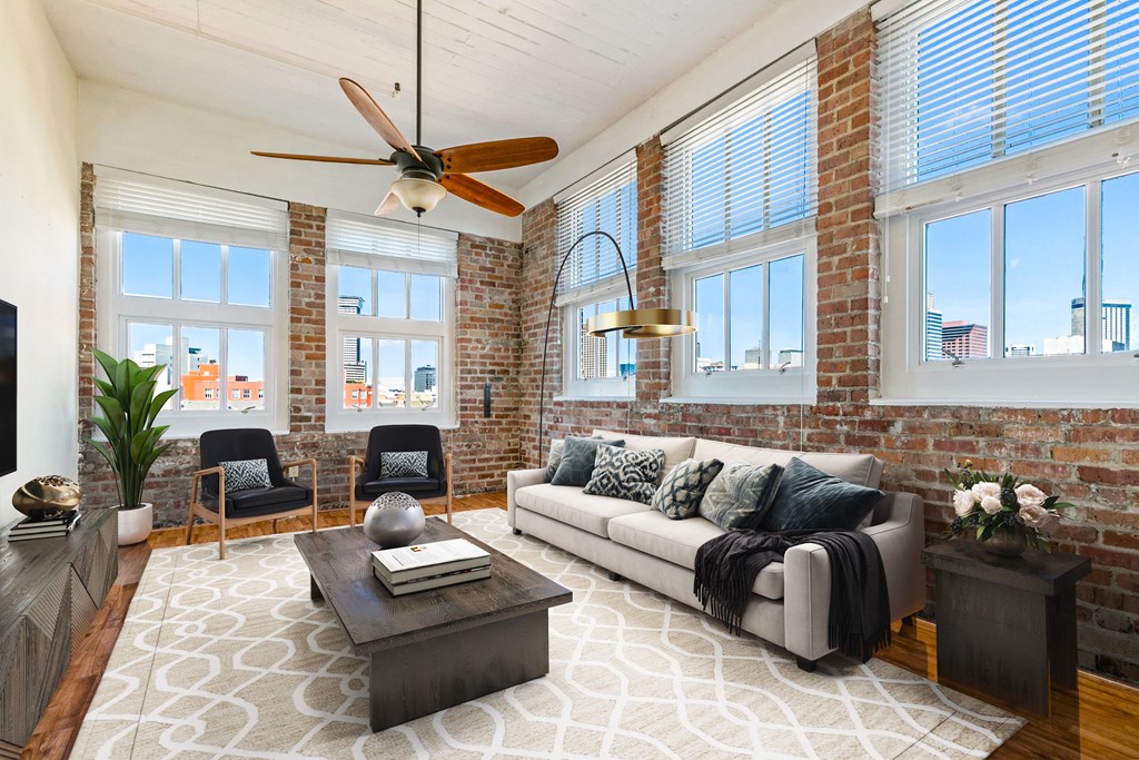 a living room with a couch and a ceiling fan and exposed brick walls