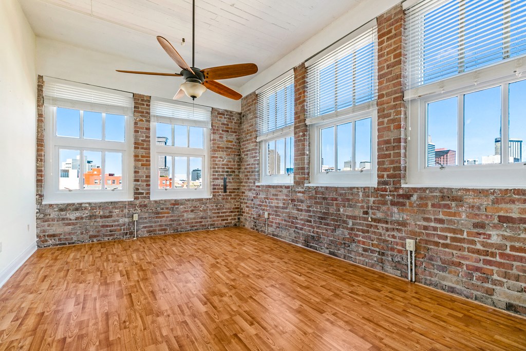 an empty living room with wood floors and brick walls and a ceiling fan