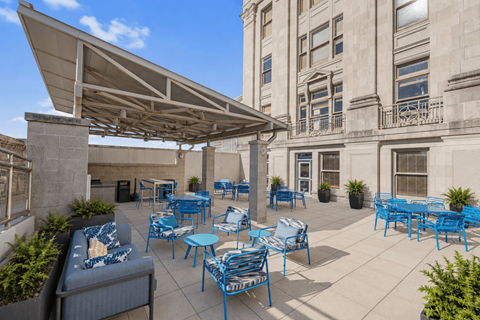 A patio with blue chairs and tables is covered by a white awning.