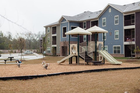 A playground with a slide and two umbrellas in front of a blue apartment building.