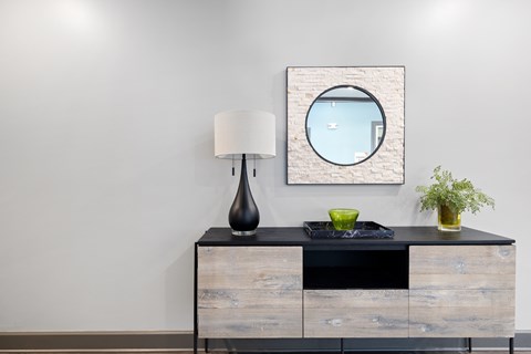 A black and wood dresser with a round mirror and a black vase on top.