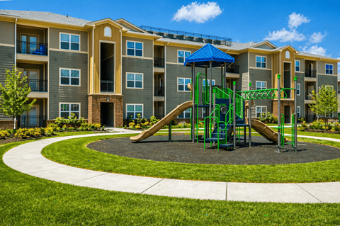 A playground with a green slide and a blue canopy is in front of a multi-story apartment building.