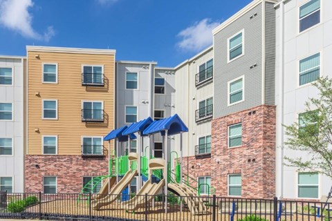 A playground with a green slide is in front of apartment buildings.