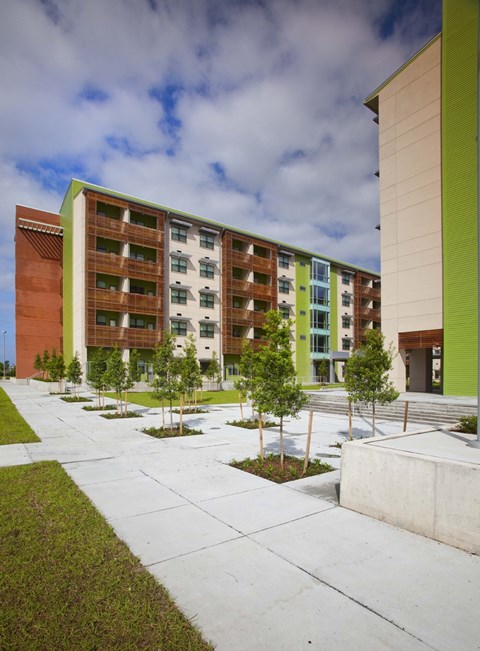A modern building with a green and brown exterior and a courtyard with trees and grass.