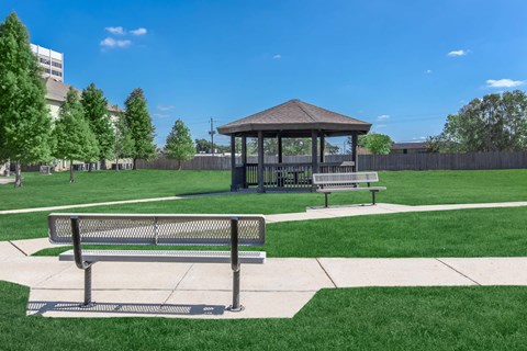 A gazebo sits in the middle of a grassy field with a bench in front of it.