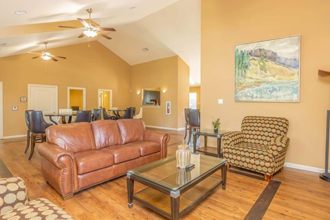 A living room with a brown leather couch, a glass coffee table, and a painting on the wall.