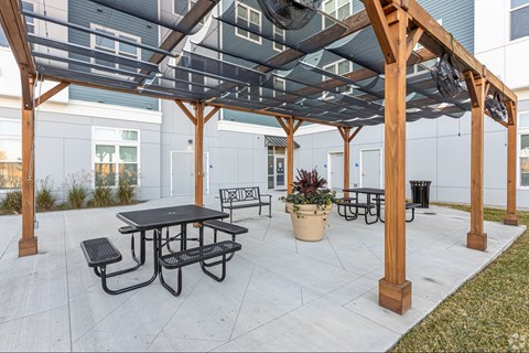 A wooden pergola with a black table and benches is set up on a patio.
