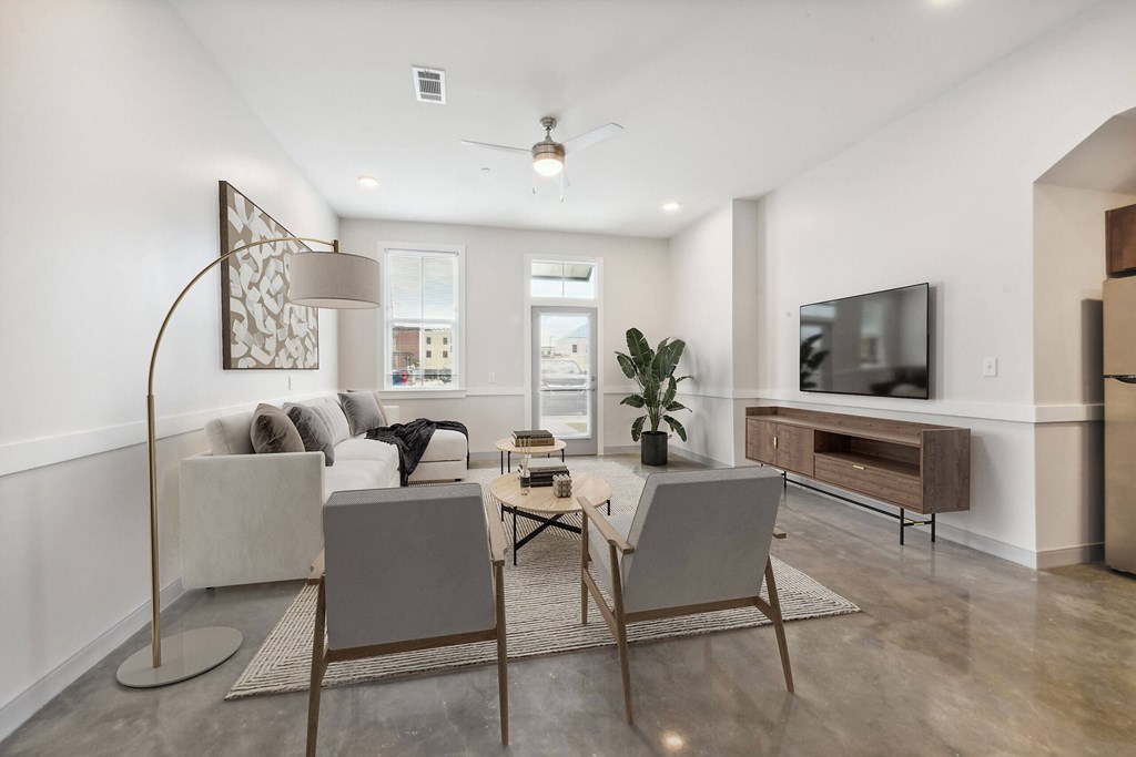 A modern living room with a grey sofa, a wooden floor, and a television on the wall.