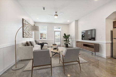 A modern living room with a grey sofa, a wooden floor, and a television on the wall.