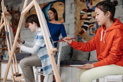 a girl painting on a canvas with other people in an art studio