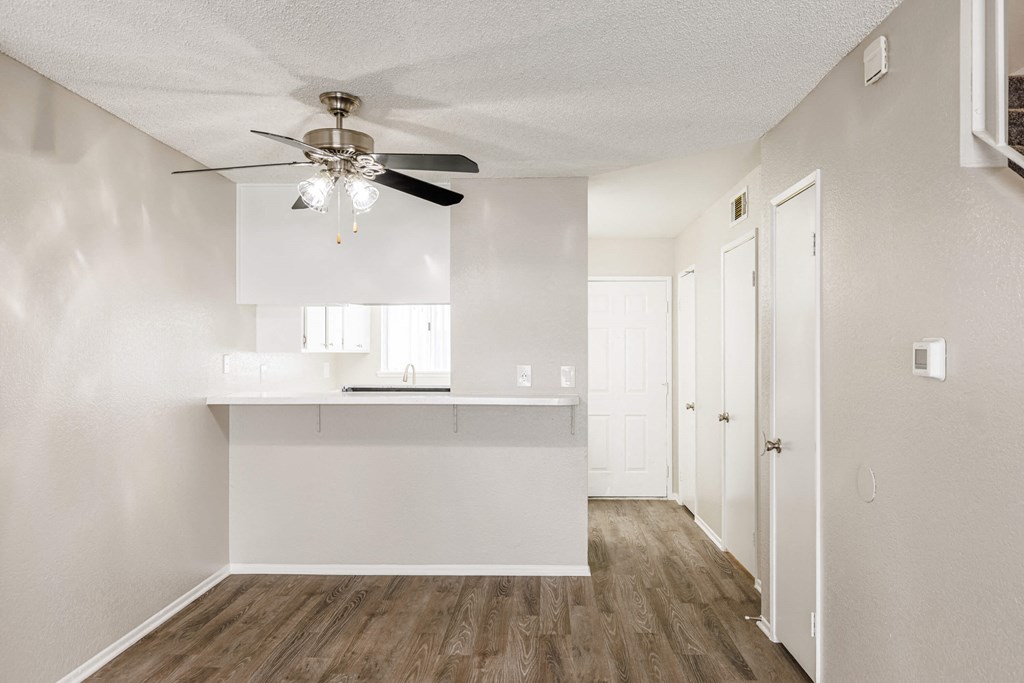 an empty living room with a ceiling fan and a white kitchen