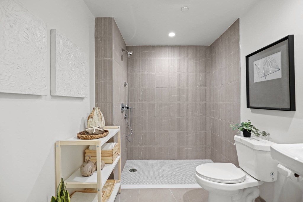 a bathroom with tiled walls and floor and a walk in shower with a glass door at The Fairfax Flats Apartments, Los Angeles, CA