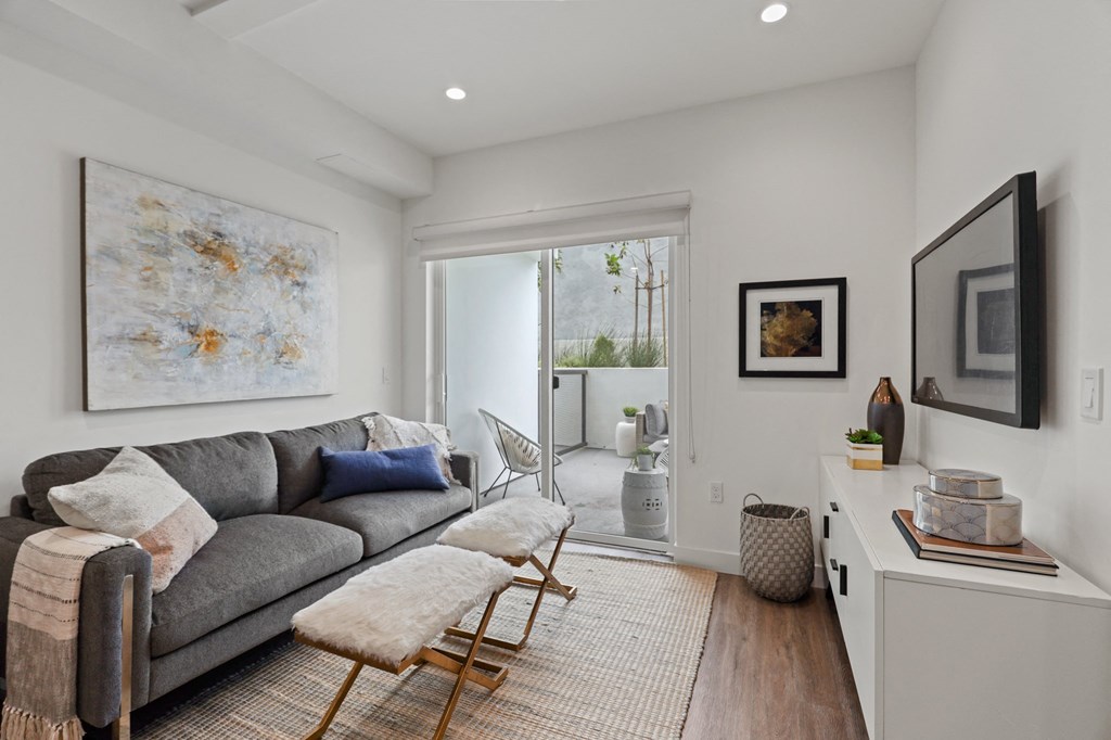 a living room with a gray couch and two stools in front of a sliding glass door at The Fairfax Flats Apartments, Los Angeles, CA