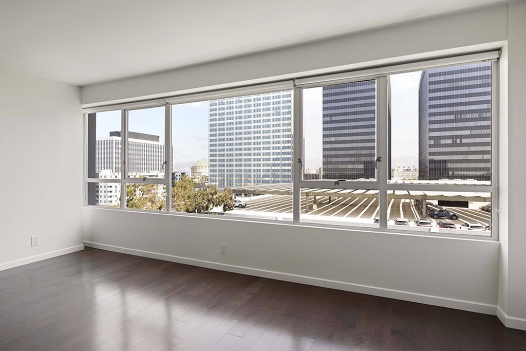 A room with a view of a parking lot and buildings outside.