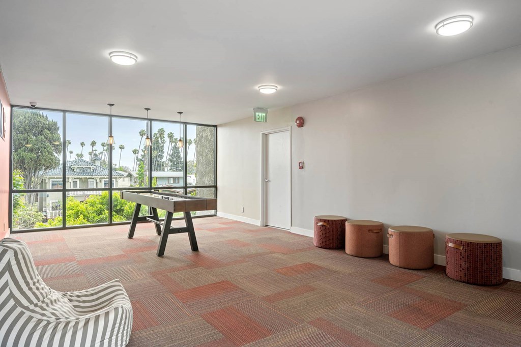 A room with a striped chair, a wooden table, and four stools at Lafayette Apartments, Los Angeles, CA