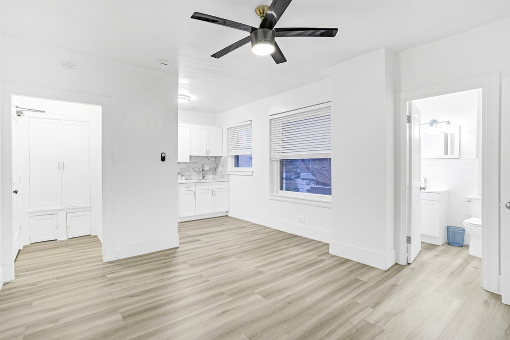 A room with a ceiling fan and light, wooden floors, and a window with blinds.