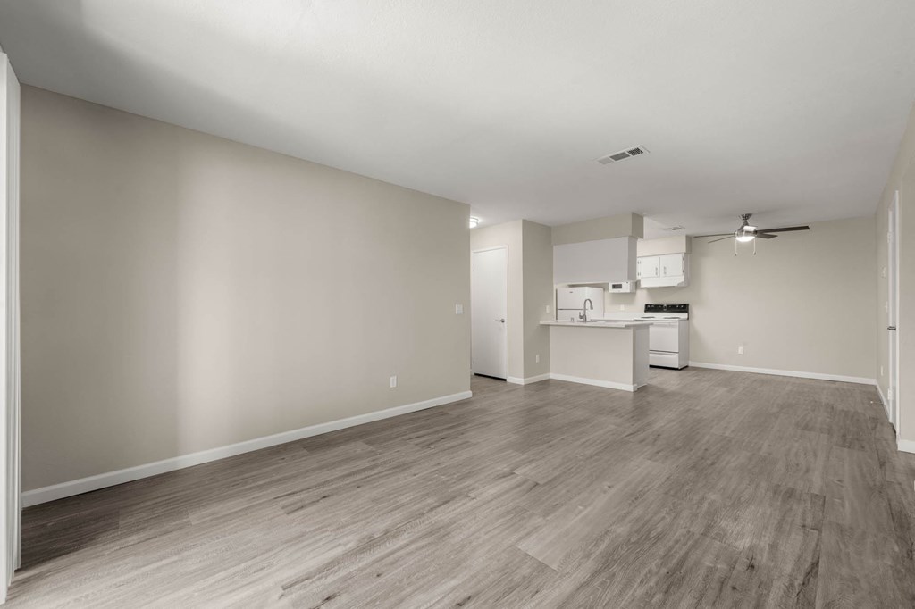 an empty living room and kitchen with wood flooring and white walls