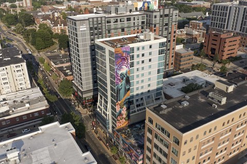 A tall building with a mural painted on the side is in the center of a cityscape.