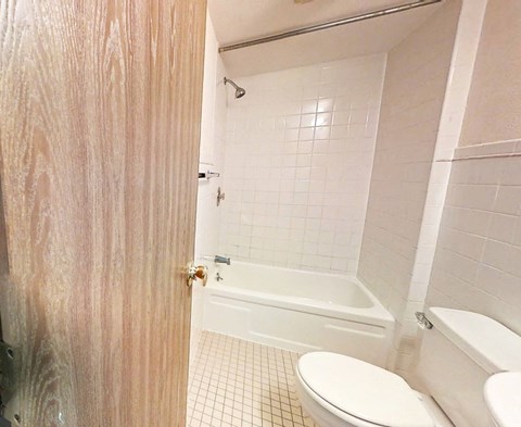 A white toilet sits in a bathroom next to a bathtub.