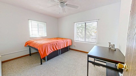 A bedroom with a bed, desk, and window.