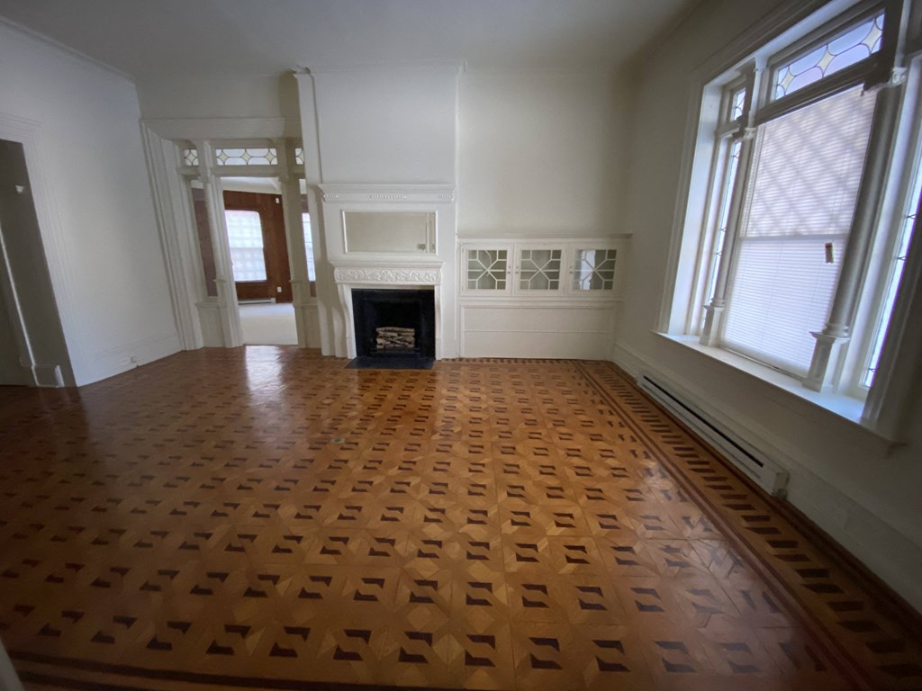 Kings Court Apartments - Front House - Living room / Wood Parquet flooring / Fireplace with Mantel / Built-in, glass-front cabinets / Stained glass transom windows / Stained glass front window