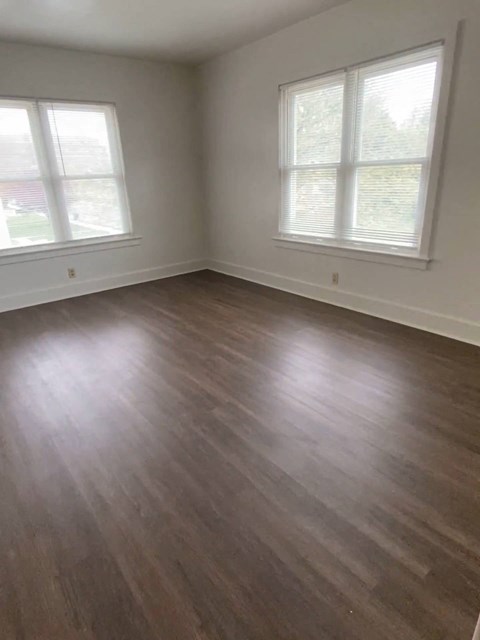 an empty living room with wooden floors and two windows