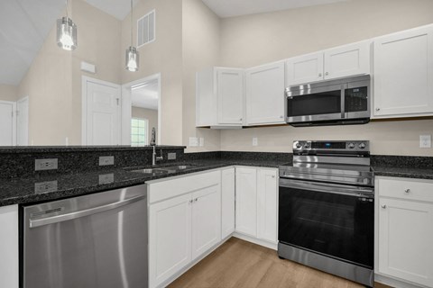 A kitchen with white cabinets and black countertops.