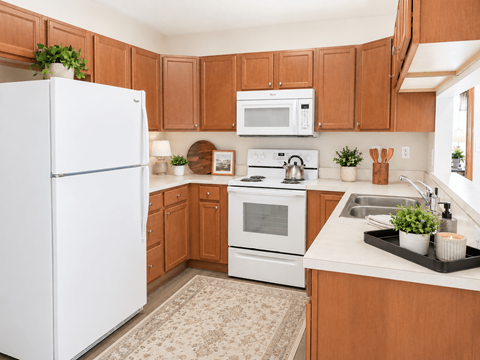 A white refrigerator stands in a kitchen with brown cabinets and a white stove.