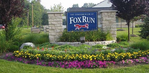 A sign that says "The Condominium at Fox Run" is surrounded by flowers.