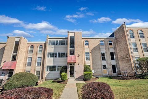 A building with a red awning and a red door is surrounded by bushes and a clear blue sky.