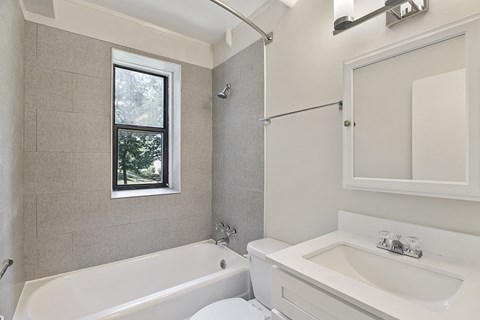 A white bathroom with a tub, sink, and window.